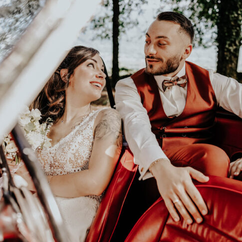 un couple de marié dans une belle voiture rouge