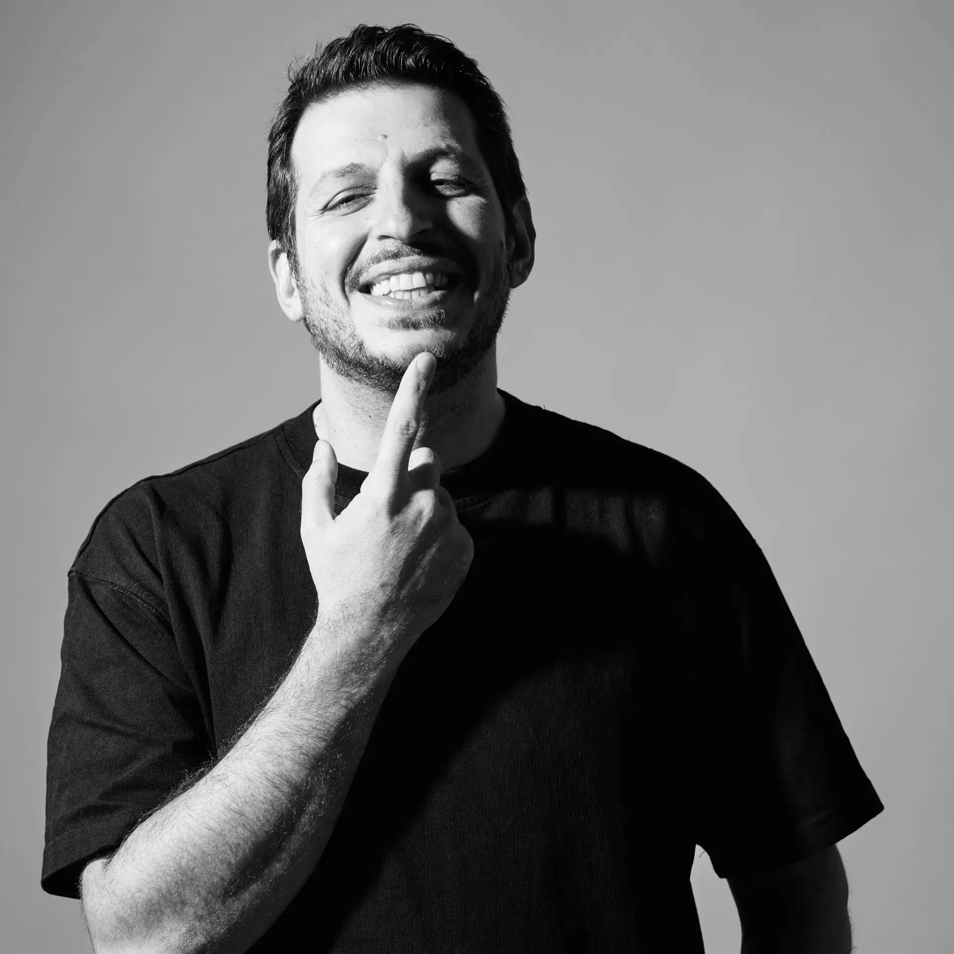 Portrait studio d&eacute;contract&eacute; en noir et blanc &agrave; Grenoble &mdash; homme sourire expressif main au menton, &eacute;clairage lat&eacute;ral sculpt&eacute; &mdash; photo CV et book Utopikphoto