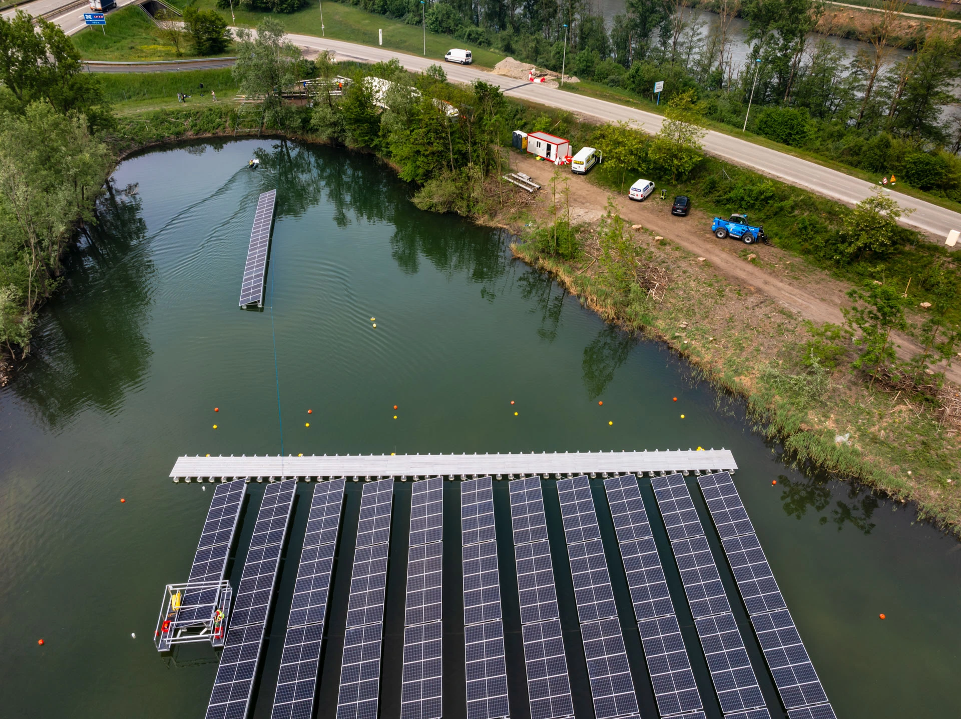 Chantier d'une centrale solaire flottante vu du ciel, avec la passerelle et une rangée en cours de remorquage